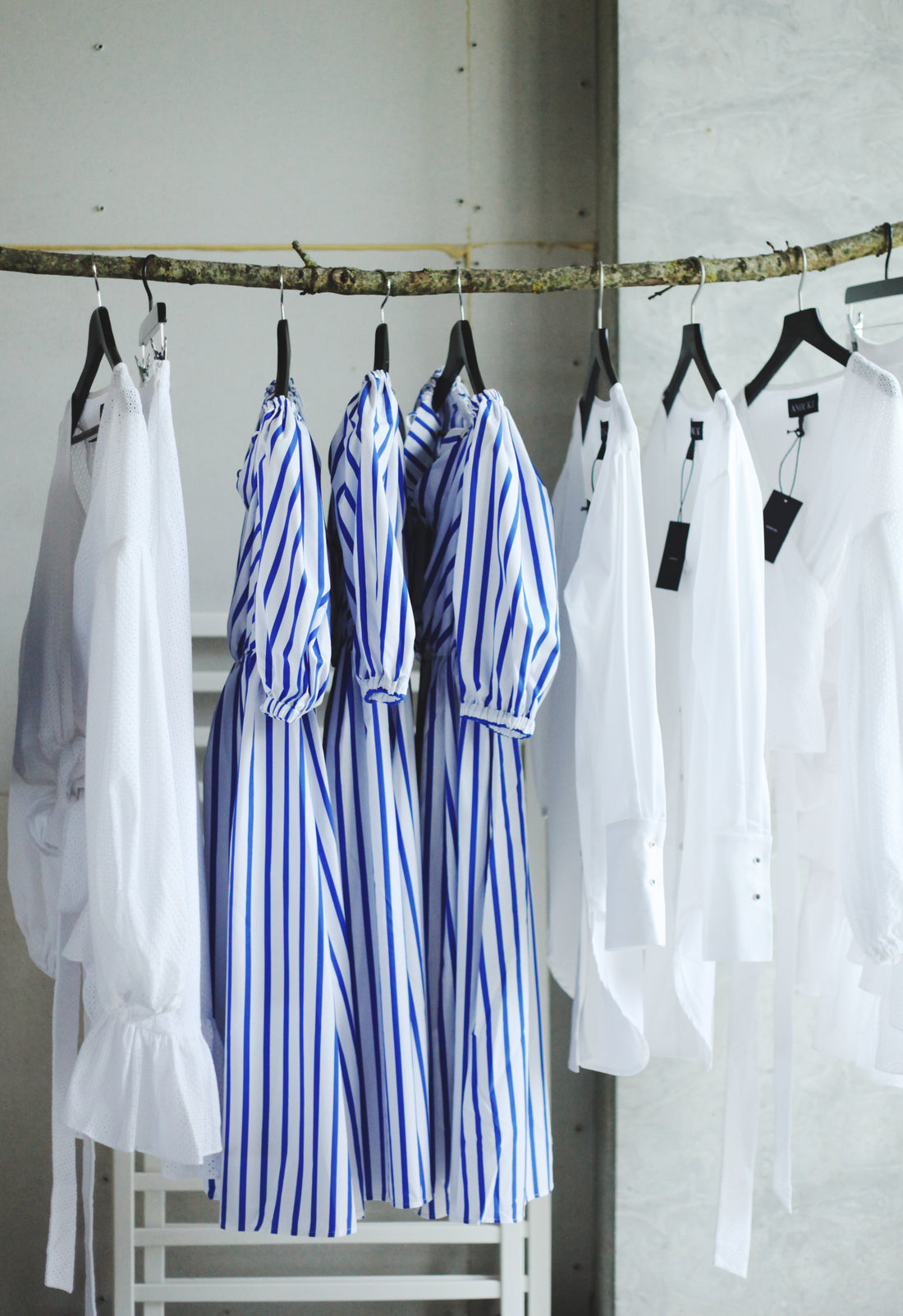 Striped dresses and white shirts hanging on a wooden branch